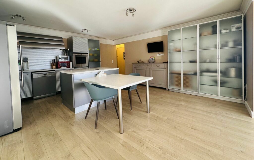Cuisine ouverte moderne avec îlot, électroménager inox, table et chaises vert canard – appartement Cap d'Ail