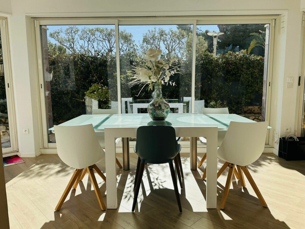 Salle à manger lumineuse, table en verre et chaises scandinaves avec vue sur le jardin – location Cap d'Ail Monaco