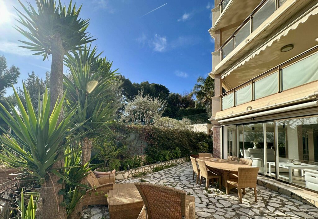 Terrasse en pierre avec mobilier en rotin et palmiers, vue sur la façade – appartement Cap d'Ail Monaco