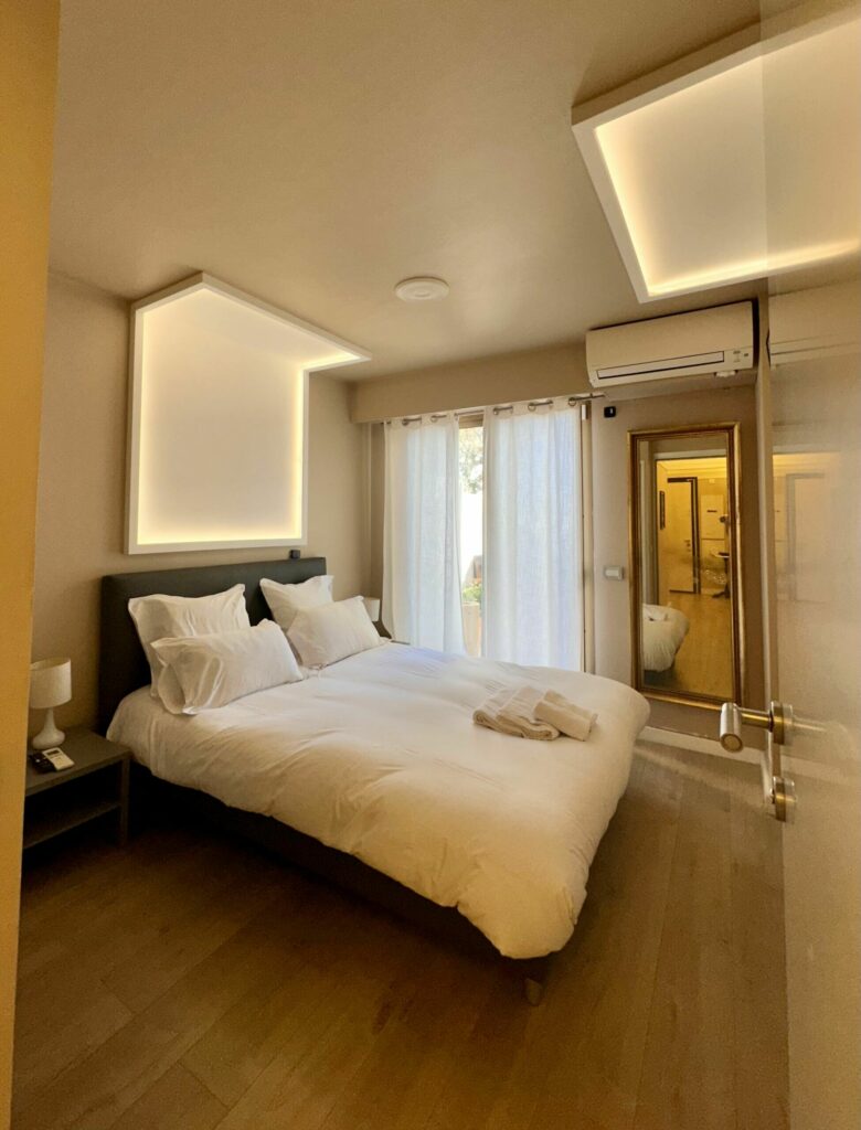 Chambre moderne avec lit double, éclairages LED géométriques, miroir doré – location saisonnière Monaco
