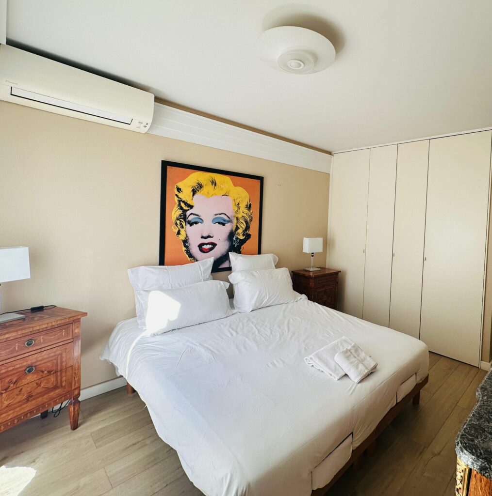 Chambre principale avec lit double, tête de lit pop art, meubles en bois classiques – location Cap d'Ail Monaco